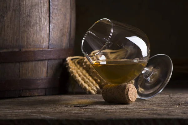 Glass of Cognac and old oak barrel defocussed — Stock Photo, Image
