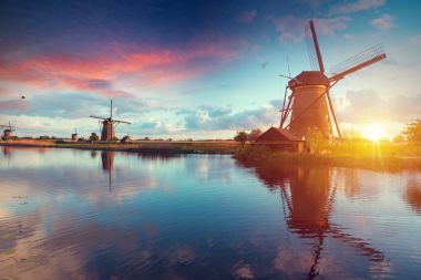 Güneş doğarken Hollanda yel değirmeni. Geleneksel Hollanda Yeldeğirmeni, yeşil çimen, renkli gökyüzü bulutlu Parmaklığa. Hollanda'da rustik panoramik manzara güneşli sabah. Kırsal sahne. Seyahat