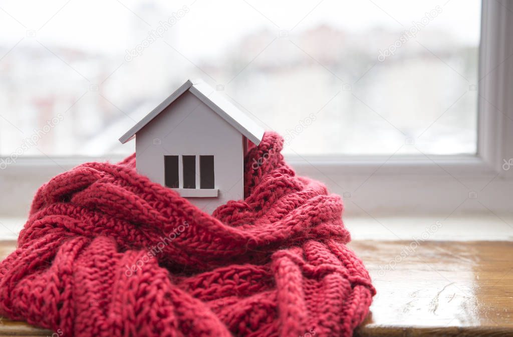 house in winter - heating system concept and cold snowy weather with model of a house wearing a knitted cap