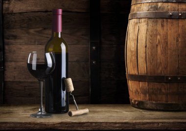 Excellent red wine bottles, wineglass, barrel and corkscrew on a rustic wooden table: traditional winemaking and wine tasting concept clipart