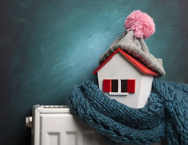 La casa en invierno - el concepto del sistema de calefacción y el tiempo frío nevado con el modelo de la casa que lleva la gorra tejida — Foto de Stock