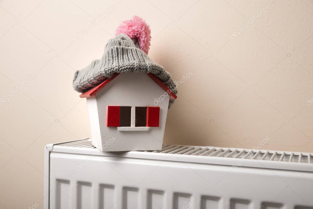 house in winter - heating system concept and cold snowy weather with model of a house wearing a knitted cap