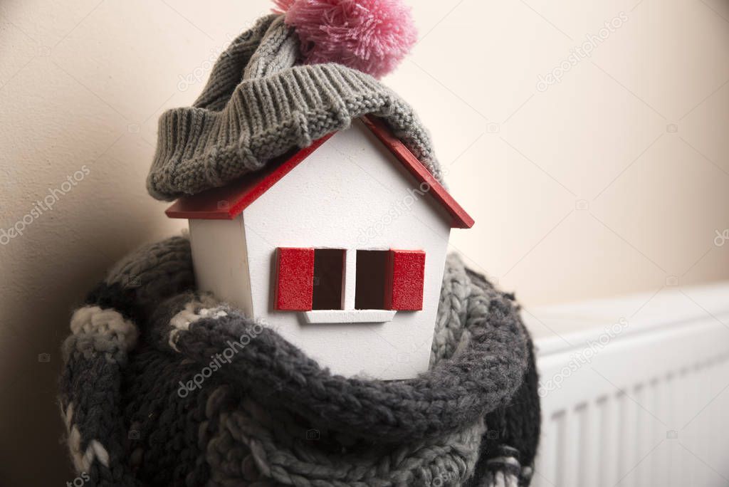 house in winter - heating system concept and cold snowy weather with model of a house wearing a knitted cap