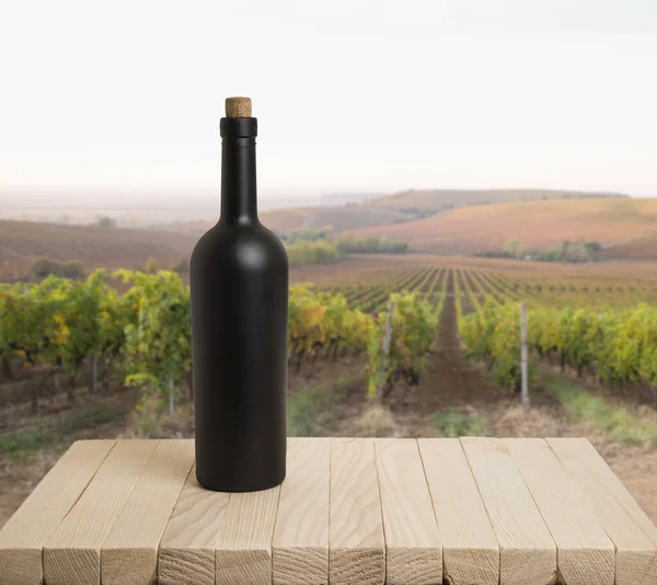 Paisaje soleado de viñedo con hojas verdes y botellas de vino en la mesa — Foto de Stock