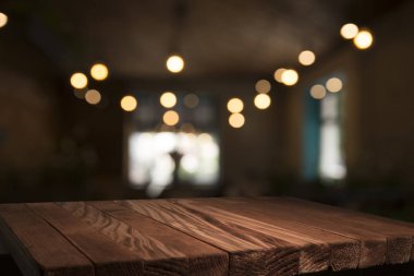 Boş kahverengi ahşap masa ve insanların yemekten hoşlandıkları, montaj için veya ürünlerinizi sergilemek için kullanılabilecek olan rezidans ışıklarının bulanık arkaplanı