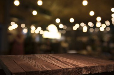 Boş kahverengi ahşap masa ve insanların yemekten hoşlandıkları, montaj için veya ürünlerinizi sergilemek için kullanılabilecek olan rezidans ışıklarının bulanık arkaplanı