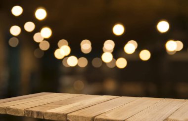 Boş kahverengi ahşap masa ve insanların yemekten hoşlandıkları, montaj için veya ürünlerinizi sergilemek için kullanılabilecek olan rezidans ışıklarının bulanık arkaplanı