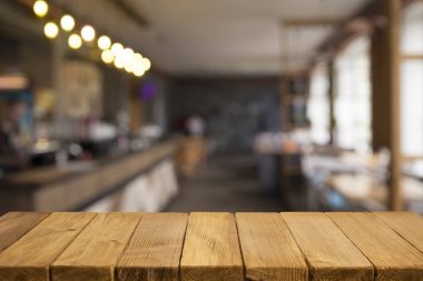 Boş kahverengi ahşap masa ve insanların yemekten hoşlandıkları, montaj için veya ürünlerinizi sergilemek için kullanılabilecek olan rezidans ışıklarının bulanık arkaplanı