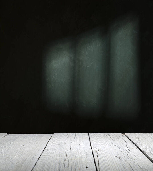 Old wood table with blurred concrete block wall in dark room background.