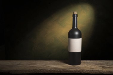 Şarap şişelerinin yanında duran barmen ya da erkek barmen bir bardak şarap tutuyor, renge bakıyor ve kadehteki şarap kokusunu alıyor..