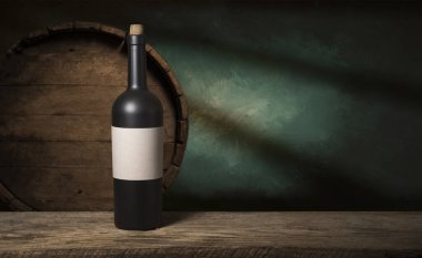 Şarap şişelerinin yanında duran barmen ya da erkek barmen bir bardak şarap tutuyor, renge bakıyor ve kadehteki şarap kokusunu alıyor..