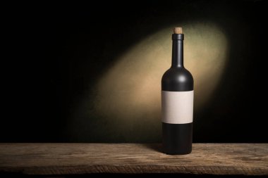 Şarap şişelerinin yanında duran barmen ya da erkek barmen bir bardak şarap tutuyor, renge bakıyor ve kadehteki şarap kokusunu alıyor..