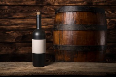 Şarap şişelerinin yanında duran barmen ya da erkek barmen bir bardak şarap tutuyor, renge bakıyor ve kadehteki şarap kokusunu alıyor..