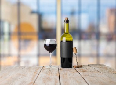 Şarap şişelerinin yanında duran barmen ya da erkek barmen bir bardak şarap tutuyor, renge bakıyor ve kadehteki şarap kokusunu alıyor..