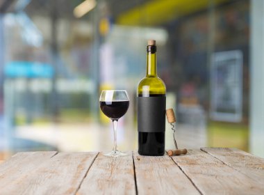 Şarap şişelerinin yanında duran barmen ya da erkek barmen bir bardak şarap tutuyor, renge bakıyor ve kadehteki şarap kokusunu alıyor..