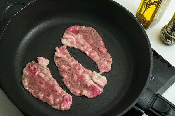beef bacon frying in a pan marbled thin beef