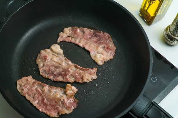 beef bacon frying in a pan marbled thin beef