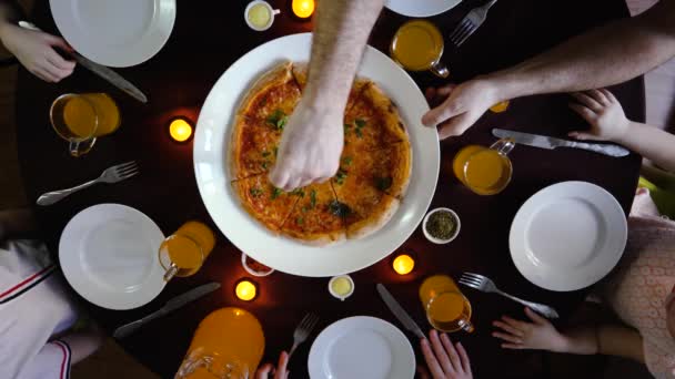 An einem runden Tisch schneidet eine Familie Pizza, Draufsicht, fünf Familienmitglieder — Stockvideo