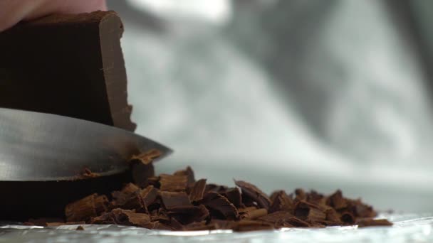 Scheggiature di cioccolato tagliate con un coltello affilato da una barretta di cioccolato su uno sfondo argento primo piano video — Video Stock