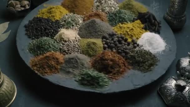 Μπαχαρικά σε ποικιλία περιστροφή σε μια στρογγυλή επιφάνεια σε σκούρο φόντο που περιβάλλεται από ανατολίτικα πιάτα, top view — Αρχείο Βίντεο