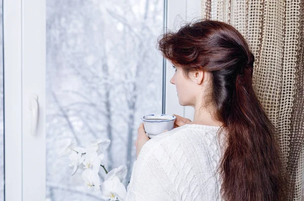雪に覆われた自然と窓の外を見るカップの女性. — ストック写真