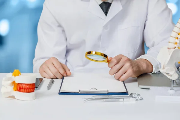 En läkare studerar en sjukdomshistoria med en förstoringsglas . — Stockfoto