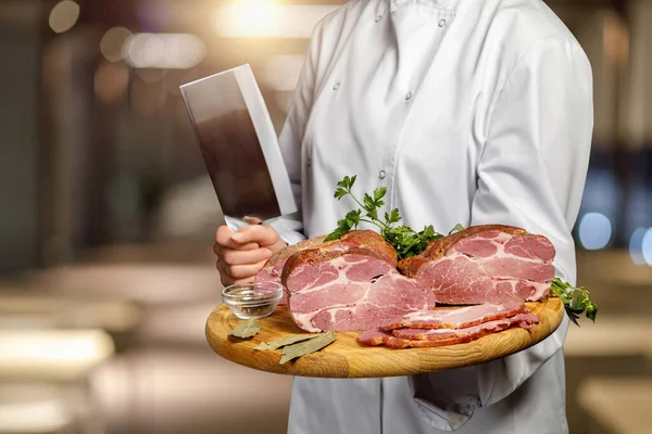 A cook shows sliced ham on a board in a restaurant.