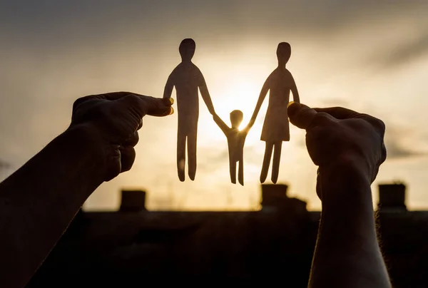 The concept of support for a young family.Hands shows a silhouette of a family on a background of the sun.
