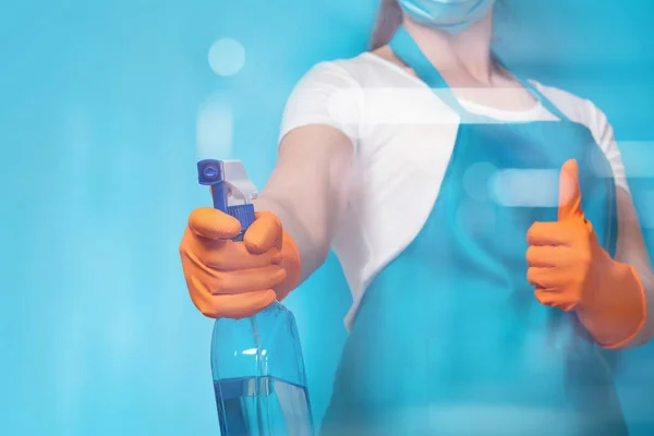 A cleaning lady in a mask and with a spray in her hands on a blue background.