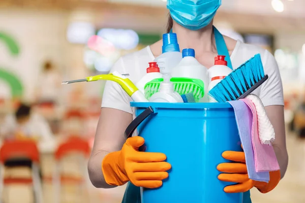 Cleaning lady in a mask with cleaning products on a blurred background.