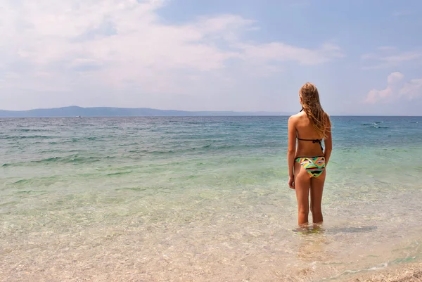 Young female in bikini facing the sea, wide view