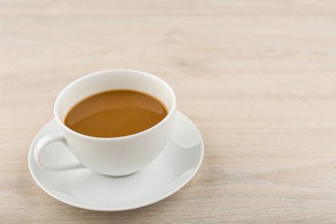 Beyaz bardakta kahve tahta bir masaya yerleştirilir