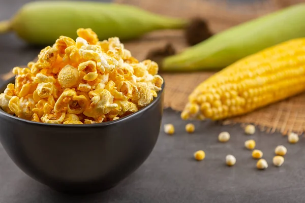 Popcorn in the black bowl and raw corn on the black table