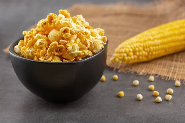 Popcorn in the black bowl and raw corn on the black table