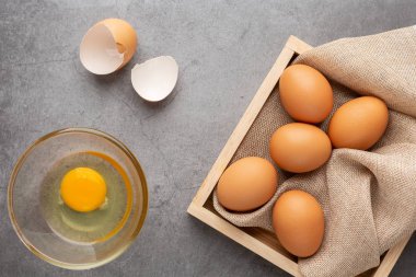 Ahşap tepside tavuk yumurtası ve siyah beton zeminde cam kase. Üst görünüm.