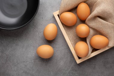 Ahşap tepside tavuk yumurtası ve siyah beton zeminde siyah cam kase. Üst görünüm.