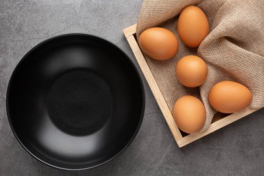 Ahşap tepside tavuk yumurtası ve siyah beton zeminde siyah cam kase. Üst görünüm.