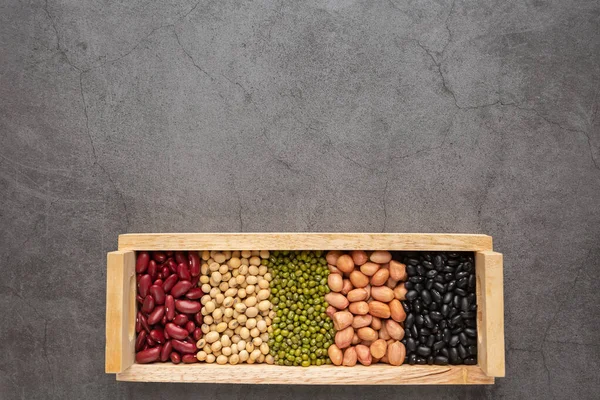 Grains or beans, red bean, black bean, green bean, soybean, peanut in the wooden tray placed on the black cement floor. Top view.