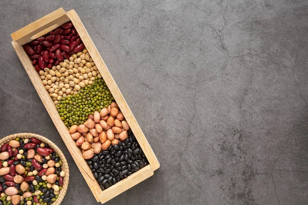 Grains or beans, red bean, black bean, green bean, soybean, peanut in the wooden tray and the wooden basket placed on the black cement floor. Top view.