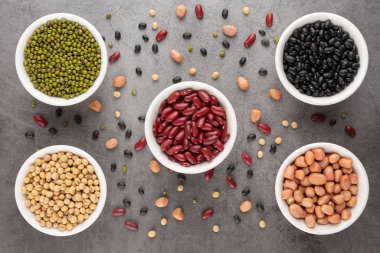 Tahıl veya fasulye, fasulye, fasulye, fasulye, fasulye, soya fasulyesi, beyaz kasede yer fıstığı, siyah çimento zemine. Üst görünüm.