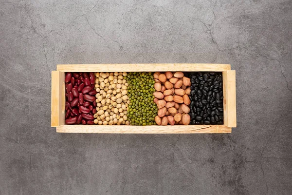 Grains or beans, red bean, black bean, green bean, soybean, peanut in the wooden tray placed on the black cement floor. Top view.