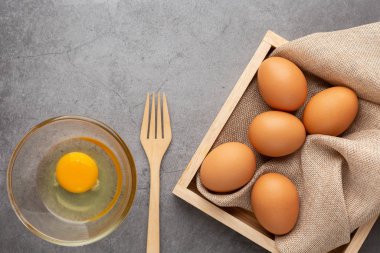 Ahşap tepside tavuk yumurtası, siyah beton zeminde çatal ve cam kase. Üst görünüm.