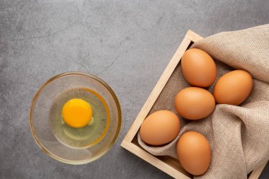 Ahşap tepside tavuk yumurtası ve siyah beton zeminde cam kase. Üst görünüm.