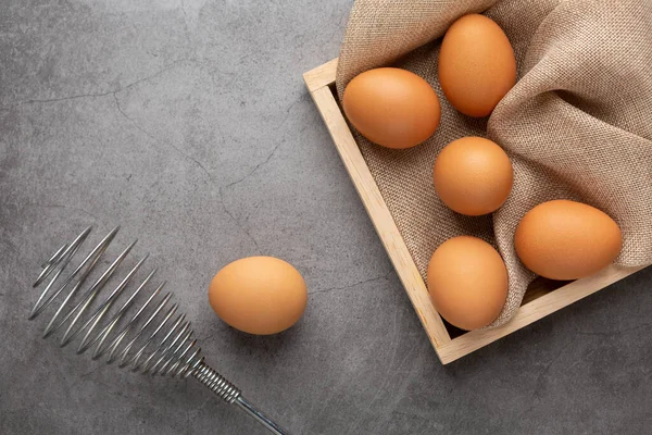 Chicken eggs and egg beater in the wooden tray on the black cement floor. Top view.