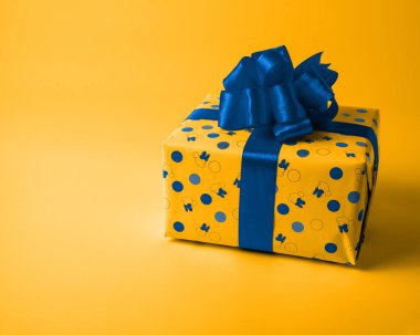 Mavi fiyonklu sarı bir kutu sevdikleriniz için bir hediyedir. Sarı arka plan. Yılın Rengi Klasik Mavi ve Saffron