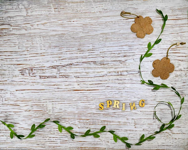 The word Spring in wooden letters on a wooden old background. Green ribbon with leaves and vintage burlap flowers — Stock Photo, Image