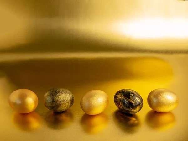 Los huevos de Pascua, pintados en oro y negro, yacen en fila sobre un fondo dorado iridiscente. Vacaciones de Semana Santa —  Fotos de Stock