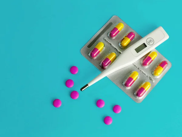 Medicina para o vírus da gripe. O conceito de medicina. Termômetro e comprimidos coloridos close-up em um fundo azul . — Fotografia de Stock