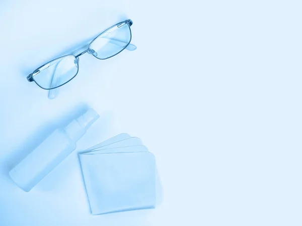 Glasses care product. Glasses, spray, napkin for glasses on light background. Blue monochrome background. Ophthalmology
