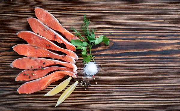 Raw red fish fillet with lemon, spices, sea salt, pepper, parsley and dill on a wooden background. Top view. — Stock Photo, Image